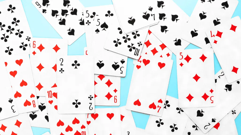 A neatly arranged discard pile rests on a polished wooden table, illuminated by warm, golden lighting. The cards are haphazardly scattered, some facing up, others turned over, creating an intriguing visual pattern. The pile sits in the foreground, with a blurred background of golf clubs and other golfing accessories, suggesting a cozy, clubhouse-like atmosphere. The overall mood is one of relaxation and strategic contemplation, inviting the viewer to ponder the game's next move.