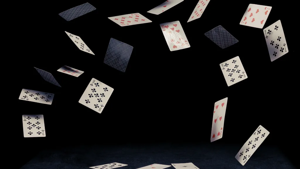 A stack of playing cards lying face-down on a weathered wooden table, with soft, natural lighting illuminating the surface. The cards are slightly worn, their edges slightly frayed, conveying a sense of well-loved use. The table has a muted, earthy tone, providing a warm, grounded backdrop. The overall composition creates a sense of anticipation and contemplation, inviting the viewer to ponder the unseen possibilities within the cards.