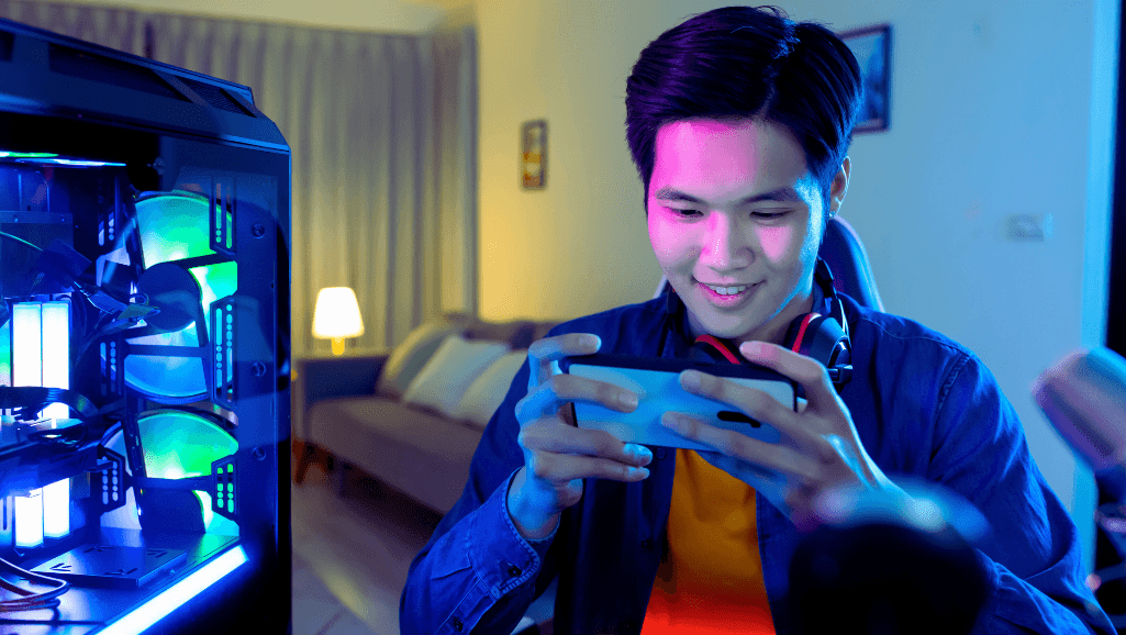 A close-up view of a smartphone screen showing a Snapchat camera lens overlay with playful, animated game elements. The screen is held in the foreground, surrounded by a blurred background of a colorful, whimsical setting. Warm, soft lighting illuminates the screen, casting a cozy glow. The lens features vibrant, cartoonish graphics such as floating bubbles, bouncing shapes, or falling confetti. The overall scene conveys a sense of joy, interactivity, and the fun of playing Snapchat games directly on the camera screen.